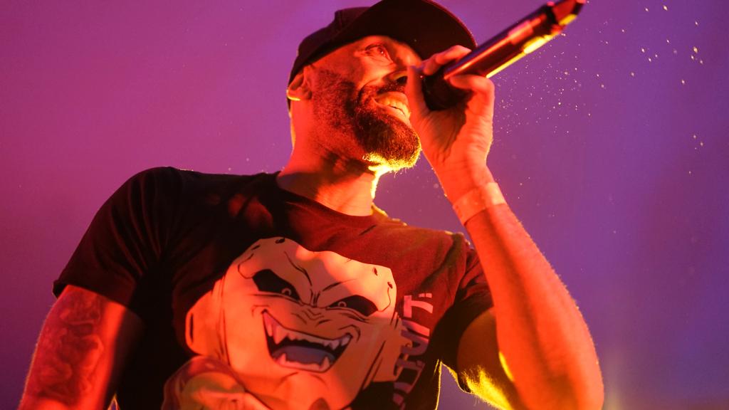 El Chojín sonríe mientras canta sobre un fondo morado con la camiseta de Boo.